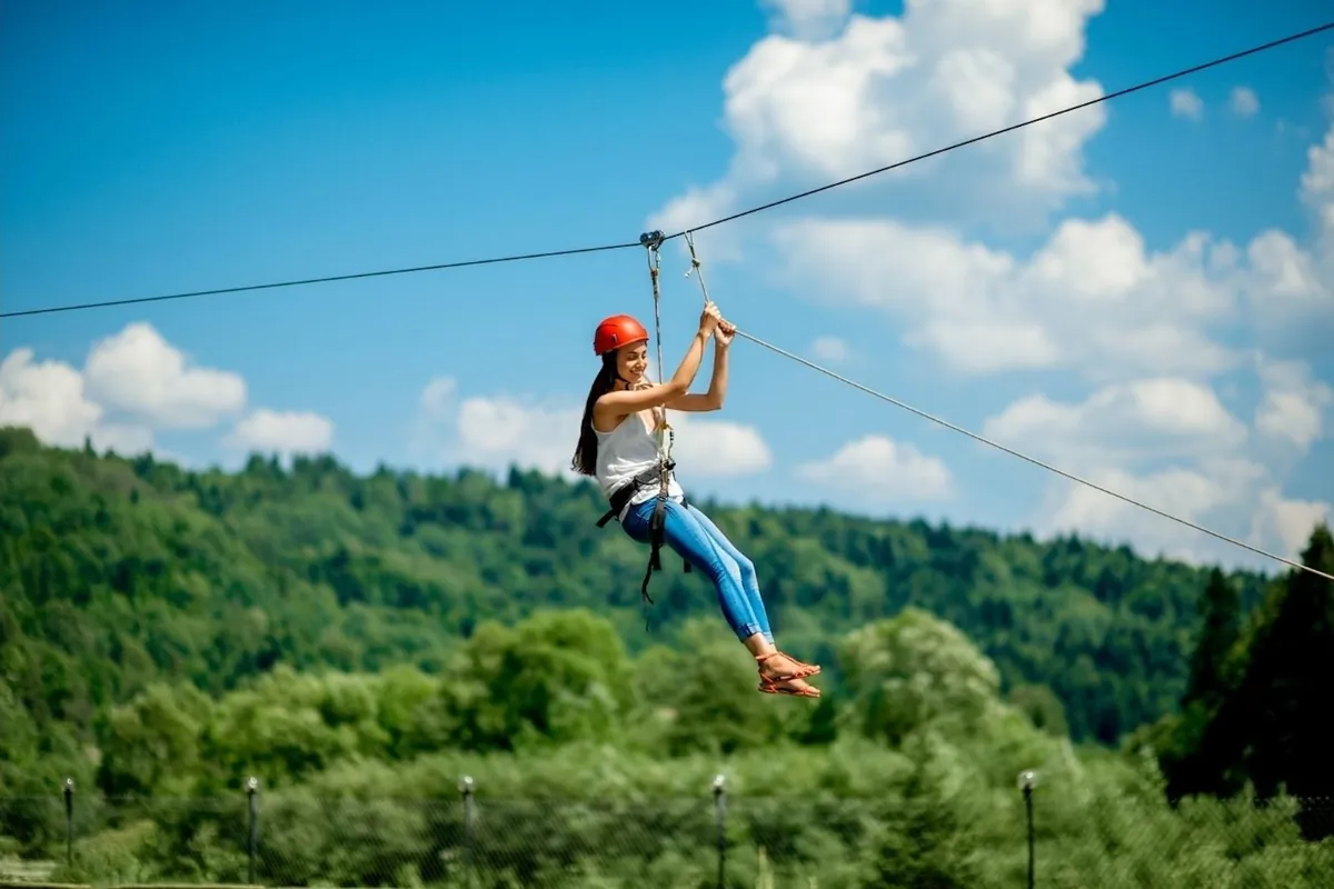 A visitor on a zipline above a green forest